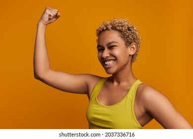 Sporty-looking Slim Female Fitness Guru In Perfect Shape Posing With Arm Up, Showing Strong Shoulder Muscles, Clenching Teeth, Dressed In Top, Wearing Nose Ring. Sport And Proper Diet