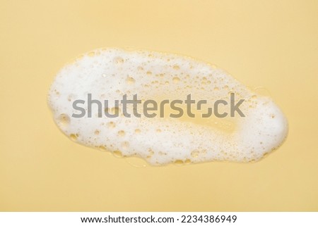 Spot of white washing foam on yellow background, top view