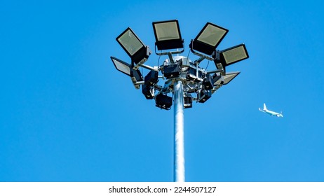 Spotlight pole with airplane and blue sky background. Floodlight pole or spotlight post with plane and sky. - Powered by Shutterstock