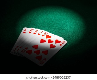 A spotlight shines on a royal flush of hearts, the winning poker hand, on a green felt table at the casino - Powered by Shutterstock