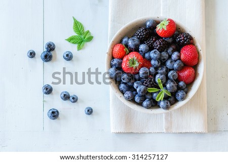 Spotted ceramic bowl with assortment berries blueberries, strawberries and blackberries at white textile napkin over wooden table. Natural day light. Top view