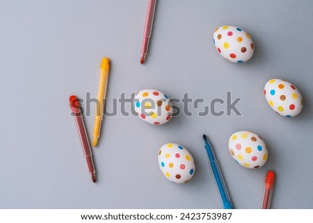 Spotty painted colorful easter eggs with coloring pens on grey background. Directly above table top shot.
