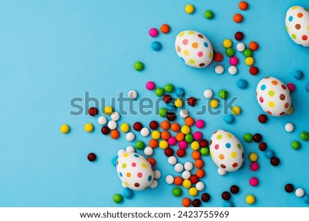 Spotty painted colorful easter eggs and colourful chocolate candies on blue background. Directly above table top shot.