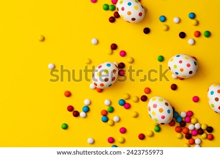 Spotty painted colorful easter eggs  and colourful chocolate beans on yellow background. Directly above table top shot.