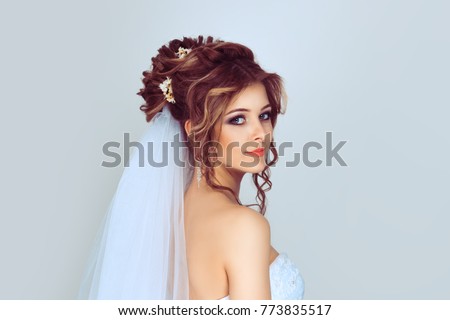 Spouse looking back. Beautiful young bride. Stylish woman fiancee with bridal hairstyle, event makeup and jewelry. Isolated light blue background with copy space