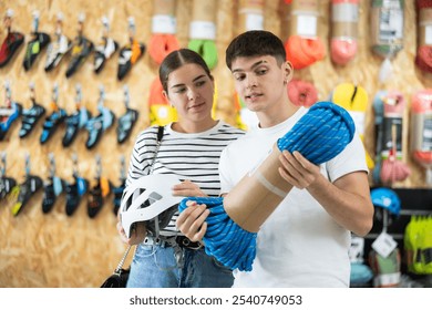 Spouses choose and buy equipment for hiking in specialized store for tourists. Buyers consider rope cable for climbing and evaluate its thickness - Powered by Shutterstock