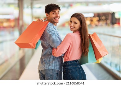 Spouses Doing Shopping Holding Hands Walking Back To Camera Carrying Paper Shopper Bags,Turning Heads And Smiling Posing In Modern Hypermarket On Weekend. Great Sales And Discounts