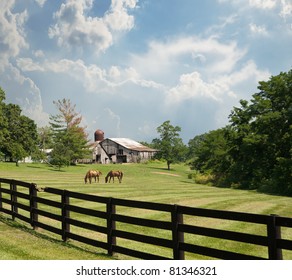 Sprawling Acreage Of Pastures Surround A Horse Farm In Kentucky, USA.  Two Horses Graze In The Pasture With An Old Rustic Barn And Silo In The Background.