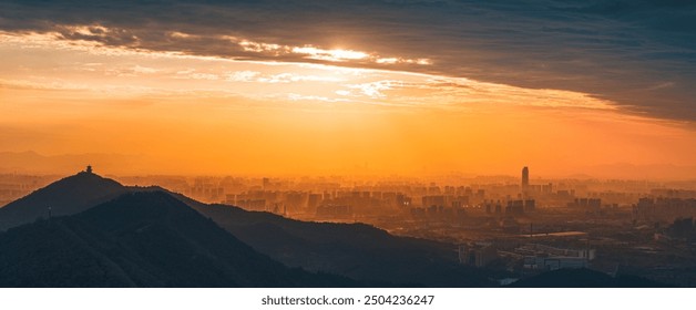 A sprawling cityscape unfolds under a dramatic sunrise, with silhouettes of high-rise buildings and dark mountains against a vibrant orange and yellow sky. - Powered by Shutterstock