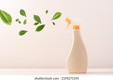 Spray Bottle With Cleaning Product On Light Background With Flying Green Leaves. Creative Eco Cleaning Concept. Environmentally Friendly Home And Office Cleaning