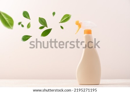 Spray bottle with cleaning product on light background with flying green leaves. Creative eco cleaning concept. Environmentally friendly home and office cleaning