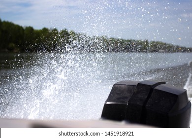 The Spray Off Of The Back Of An Old Bass Fishing Boat. The Water Was Blue And The Spray Was White. The Tree Line Flowed With The Horizon Line And One Can Notice The Wake Of The Boat In The Water.