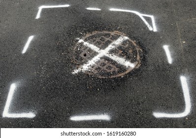 Spray painted white X on manhole cover surrounded by spray painted white lines.