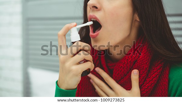 Spray for sore throat. Photo of a woman who\
treats her throat with a spray and sprinkles it in her mouth. The\
concept of health and\
disease.