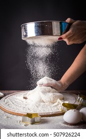 Spread the flour through a sieve on the dough. On a black background.