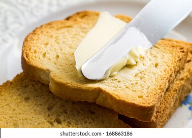 Spreading butter with a knife on sliced brown bread.