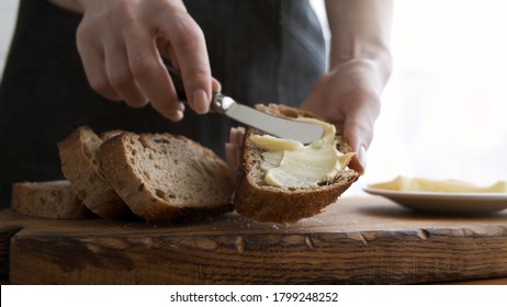 Spreading butter on sourdough bread. Female hand holding piece of bread and smearing organic butter on it