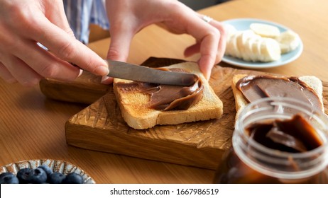 Spreading chocolate nut butter on toasted bread. Female hands smear chocolate spread on sandwich bread. Preparing lunch or breakfast
