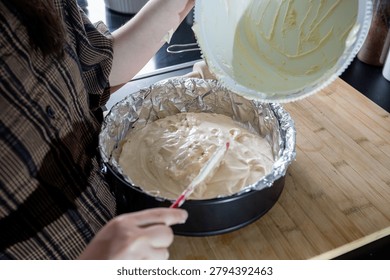 Spreading and leveling sponge cake batter in a foil-lined springform pan with a red spatula in a modern marble kitchen, finishing the batter before baking.