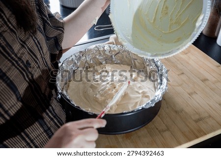 Spreading and leveling sponge cake batter in a foil-lined springform pan with a red spatula in a modern marble kitchen, finishing the batter before baking.