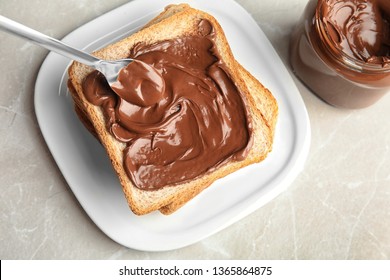 Spreading sweet chocolate cream onto toast on table, top view