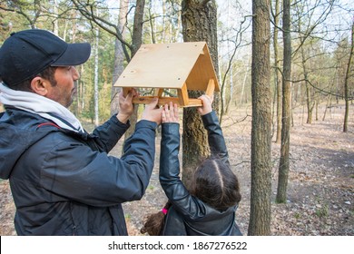 In The Spring Afternoon In The Forest, Dad And Daughter Hang A Bird Feeder On A Tree.