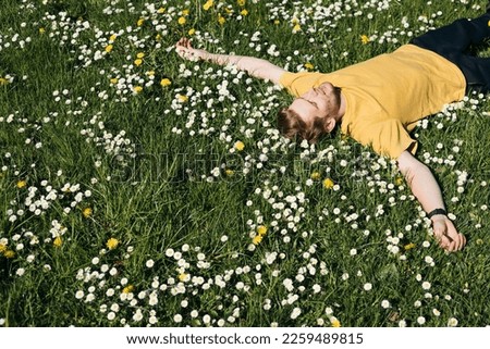 Spring allergies. A Young man sneezing amidst a blooming flowers, symbolizing spring allergies. Young male laying in green grass. Spring fatigue sleep and calm nap in allergy season. Great resignation