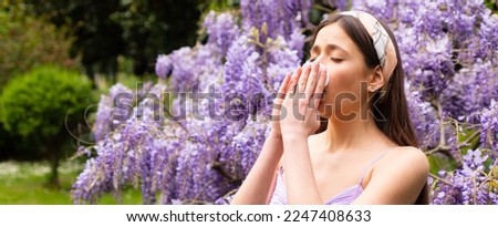 Spring allergy, flu. Banner. Sick woman sneezing covering nose with a wipe in a park. Spring allergy concept. Fashionable youth style. Allergic people. Among blooming trees and flowers in park.