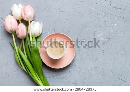 Spring background with flowers, a cup of coffee and a bouquet of pink and white tulips on colored table background with place for text. Copy space top view.