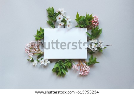 Spring background with paper sheet. Beautiful fresh flowers and leaves on gray background.