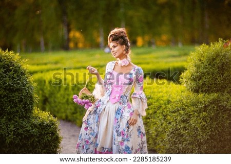 Spring Beautiful romantic girl with perfect hairstyle standing in  garden with basket of pink flowers. Dreaming queen in fairy beautiful vintage dress posing.Fairytale art work.