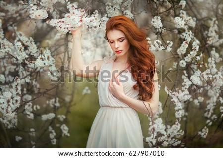 Spring Beautiful romantic red haired girl standing in blooming garden. Tenderness Young model looking down
