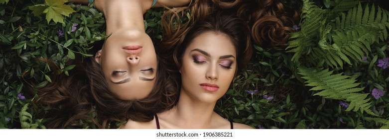 Spring Beauty Portrait. Fashionable twins models with perfect make-up and hairstyle lying on flower meadow background. Portrait shot of two gorgeous women in evening dresses with perfect look, posing