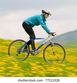 Spring bike riding - woman downhill on bike in dandelion (intentional motion blur)