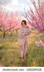 in spring, in a blooming peach garden, a woman in a pink jumpsuit with a wicker basket is posing - Shutterstock ID 1583209528