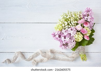 Spring bouquet of lilies of the valley, pink lilacs, daisies, viburnum flowers with lace ribbon on a white wooden background, space for text. - Powered by Shutterstock