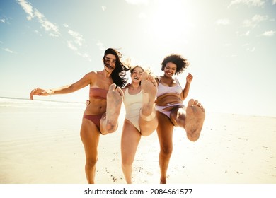 Spring break fun. Group of playful female friends standing on one leg while wearing swimwear at the beach. Carefree young women laughing cheerfully and enjoying their vacation. - Powered by Shutterstock