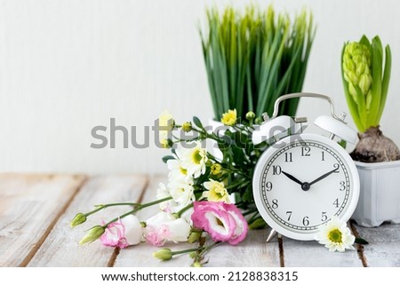 Spring change, Daylight Saving Time concept. White alarm clock and flowers on the wooden table. Copy space for text