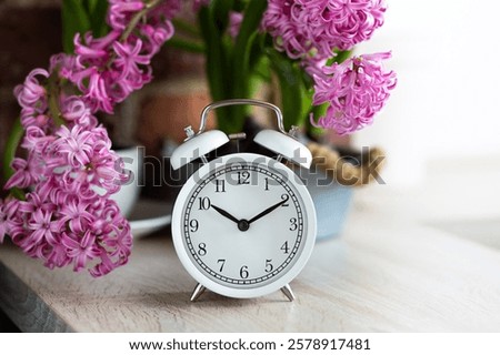 Spring change, Daylight Saving Time concept. White alarm clock and hyacinth flowers on the wooden table. Springtime home gardening, hobby, leisure. Copy space for text
