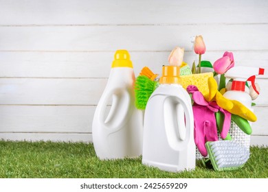 Spring cleaning background. Set of cleaning supplies, bottles, accessories and stuff with spring flowers in basket on white wooden green garden grass background copy space