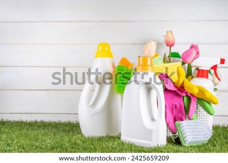 Spring cleaning background. Set of cleaning supplies, bottles, accessories and stuff with spring flowers in basket on white wooden green garden grass background copy space