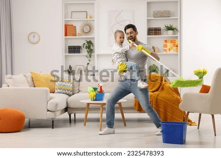 Spring cleaning. Father and daughter singing while tidying up together at home