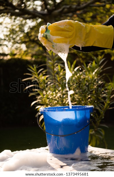 Spring Cleaning outside with big yellow cleaning
gloves, water, soap and a big blue bucket with soap. Cleaning the
table. Soap Foam on the table. Hands in bucket. Holding and
wringing cleaning
sponge.