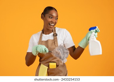 Spring Cleanup. Smiling African American woman in apron poses with cleaning supplies, detergent and feather duster, showcasing concept of cleanliness and hygiene. Housekeeping chores - Powered by Shutterstock