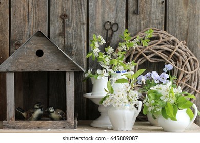 Spring Composition With Blooming Branches Of Cherry, Pear, Hawthorn In White Porcelain, China Jug, Creamer, Pitcher, Aged Bird Feeders, Vintage Pair Birds Figure, Wooden Wreath, Rusty Key, Scissors