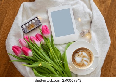 Spring composition with cup of coffee, beautiful bouquet of pink tulips, white sweater and e-reader with cope space, concept of spring and comfort. Feminine aesthetics lifestyle background.