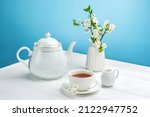 Spring composition with a teapot, a cup of tea and a blossoming cherry branch on a blue background.