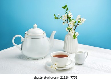 Spring composition with a teapot, a cup of tea and a blossoming cherry branch on a blue background. - Shutterstock ID 2122947752