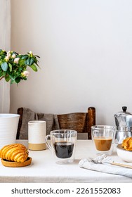 Spring cozy breakfast concept. Two mugs with coffee and milk, croissants, plant with flowers, creamer, coffee pot, jam