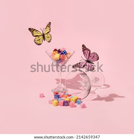 Spring creative layout with colorful butterflies  and martini glasses with dices on pastel pink background. 80s or 90s retro fashion aesthetic  concept. Minimal romantic cocktail idea.
